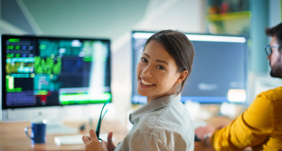 woman sitting at a computer looking behind as she is coding