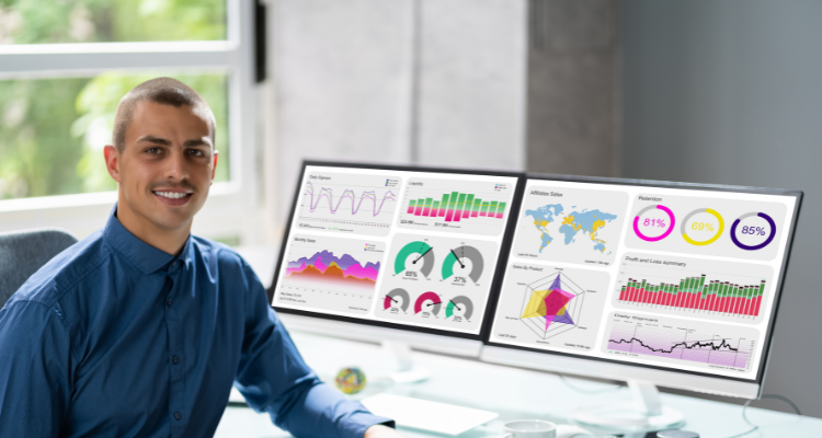 young male sitting at computer with two screens of data analytics dashboards