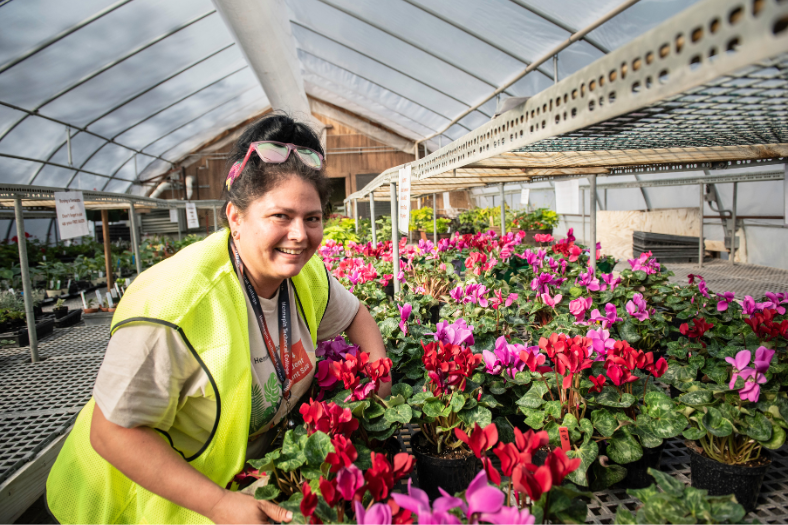 A Landscape and Horticulture student poses in a greenhouse with a variety of hanging baskets.