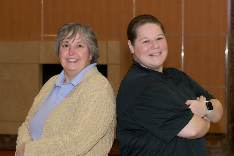 Cheryl Davis and Nora Falling pose back-to-back. Both are smiling and have their arms crossed over their chests in a classic power stance.