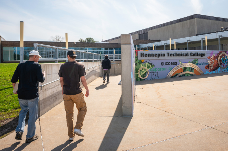 Students walking up the ramp to the Hennepin Tech Eden Prairie Campus. The Campus mural appears to the right.